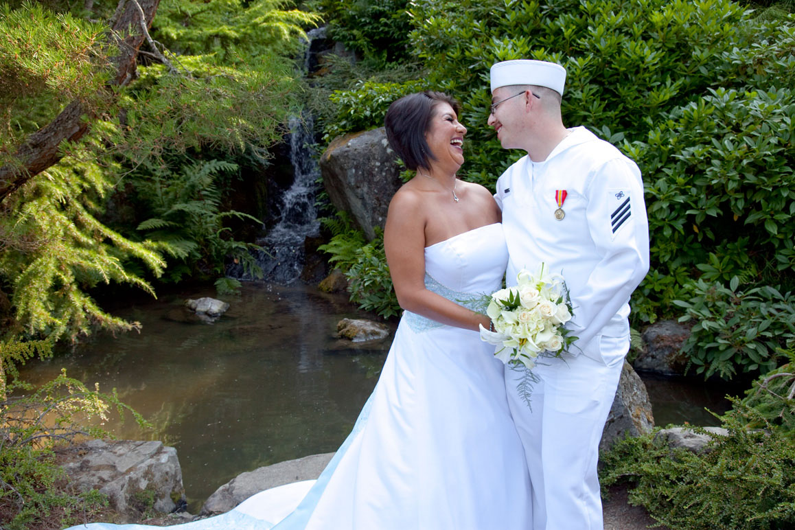Wedding at Kubota Gardens in Seattle Bride with groom in Navy uniform hugging next to waterfall at Kubota Gardens